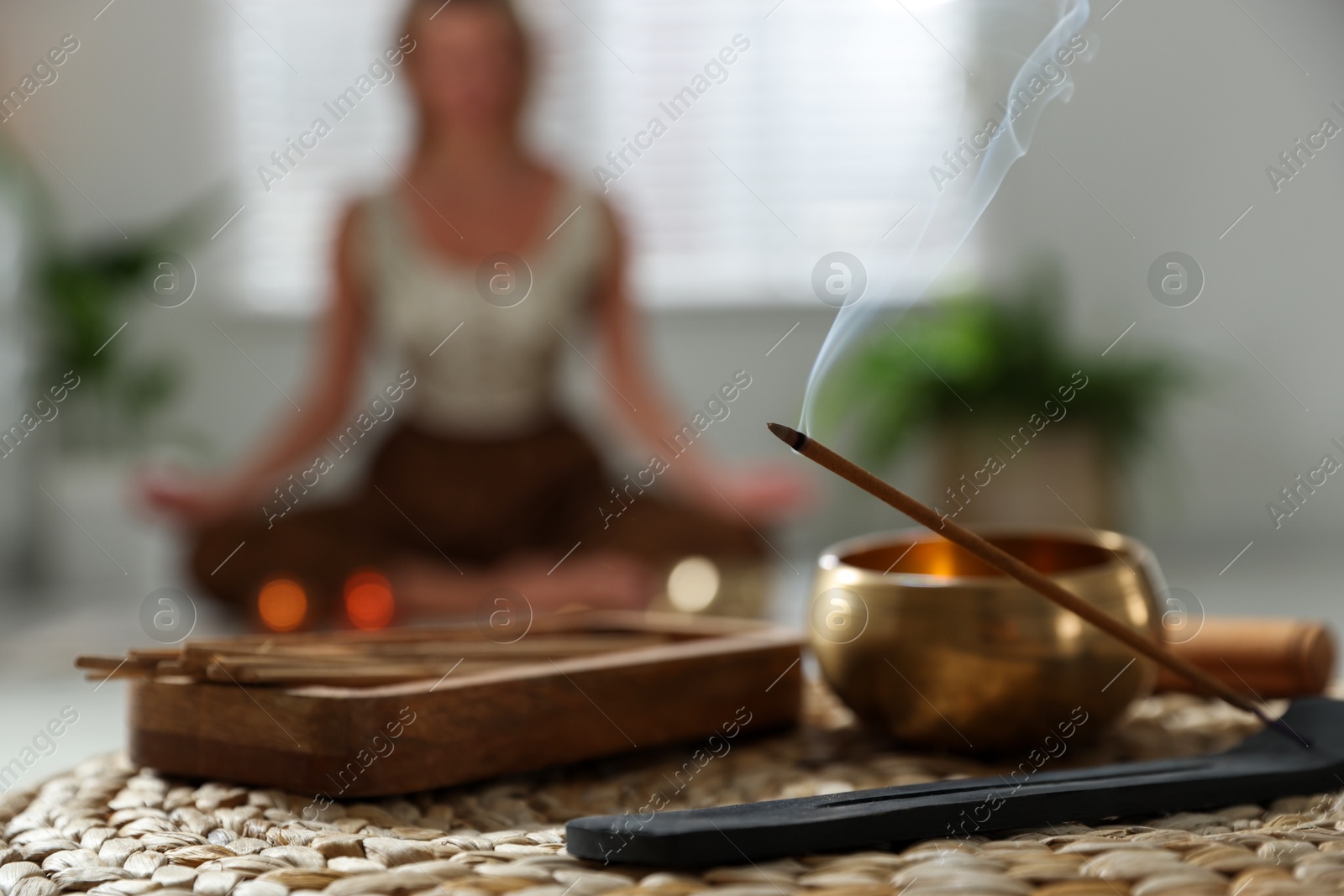 Photo of Incense stick smoldering in holder and tibetan singing bowl indoors, selective focus