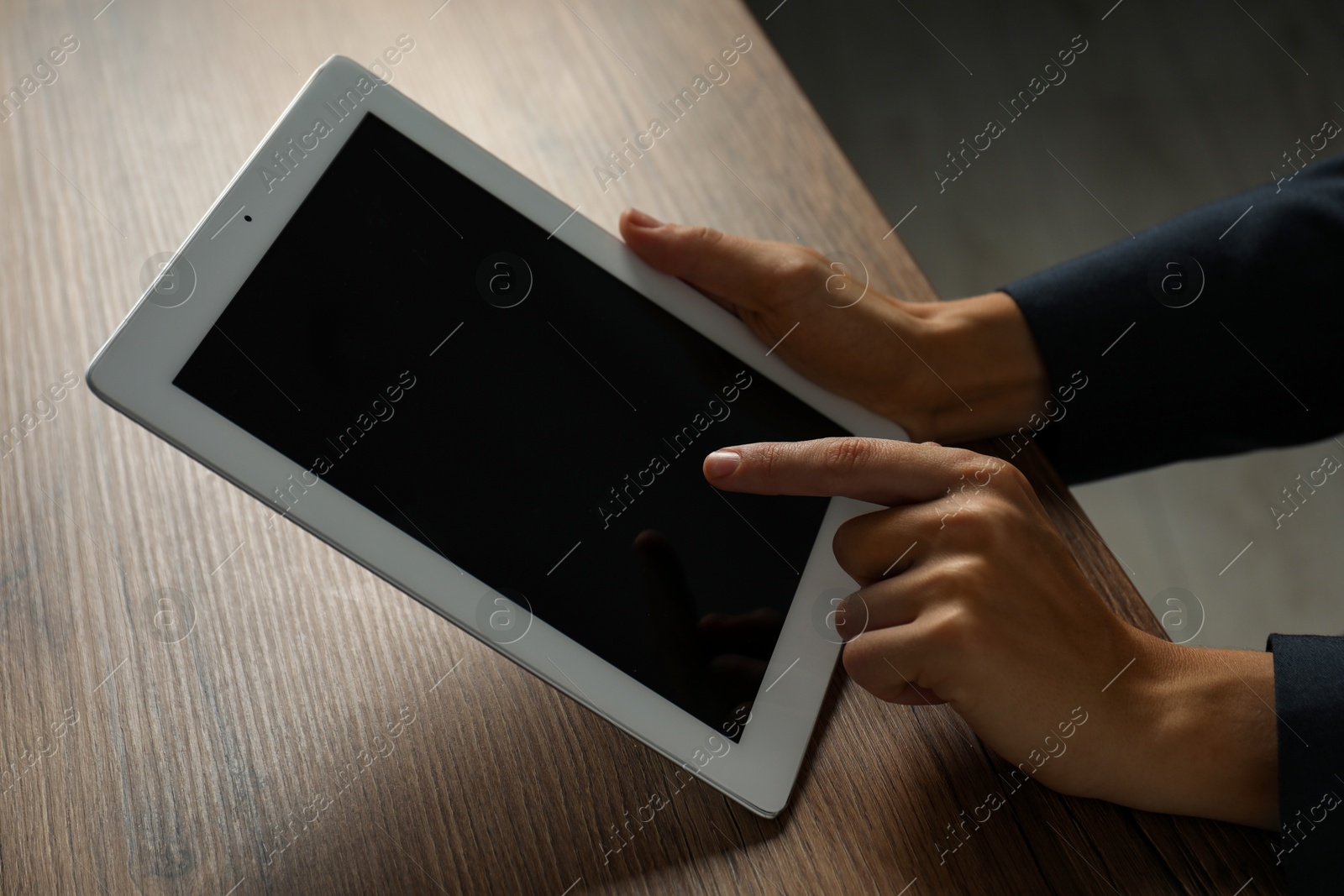 Photo of Businesswoman using tablet at wooden table indoors, closeup. Modern technology