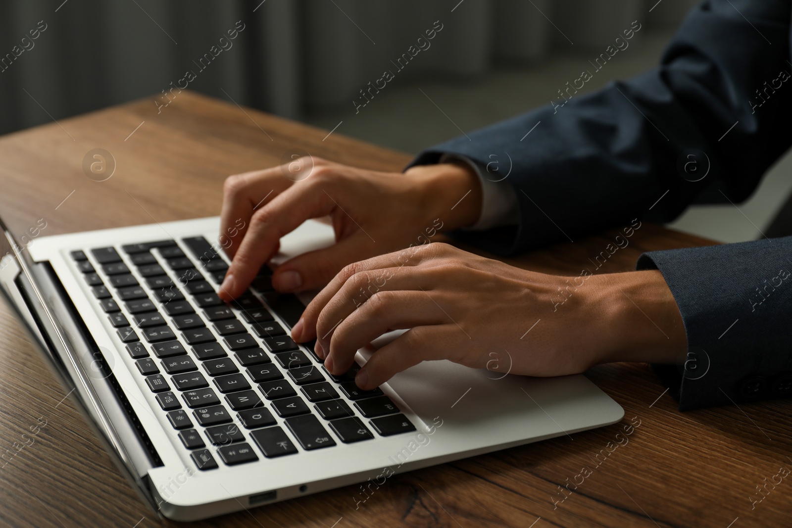 Photo of Businesswoman using laptop at wooden table indoors, closeup. Modern technology