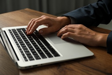 Photo of Businesswoman using laptop at wooden table indoors, closeup. Modern technology