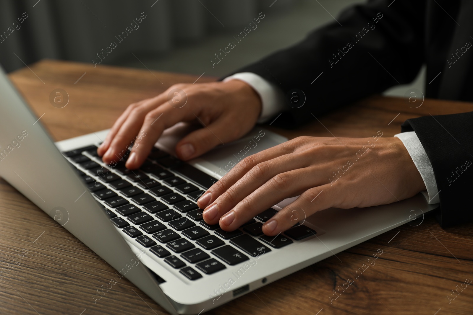 Photo of Businesswoman using laptop at wooden table indoors, closeup. Modern technology