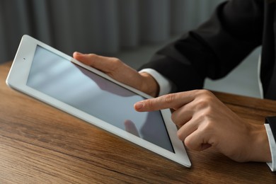 Photo of Businesswoman using tablet at wooden table indoors, closeup. Modern technology