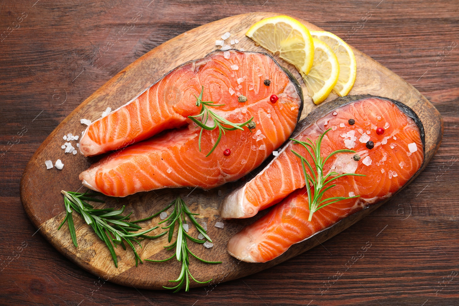 Photo of Fresh raw salmon steaks with spices, lemon and rosemary on wooden table, top view