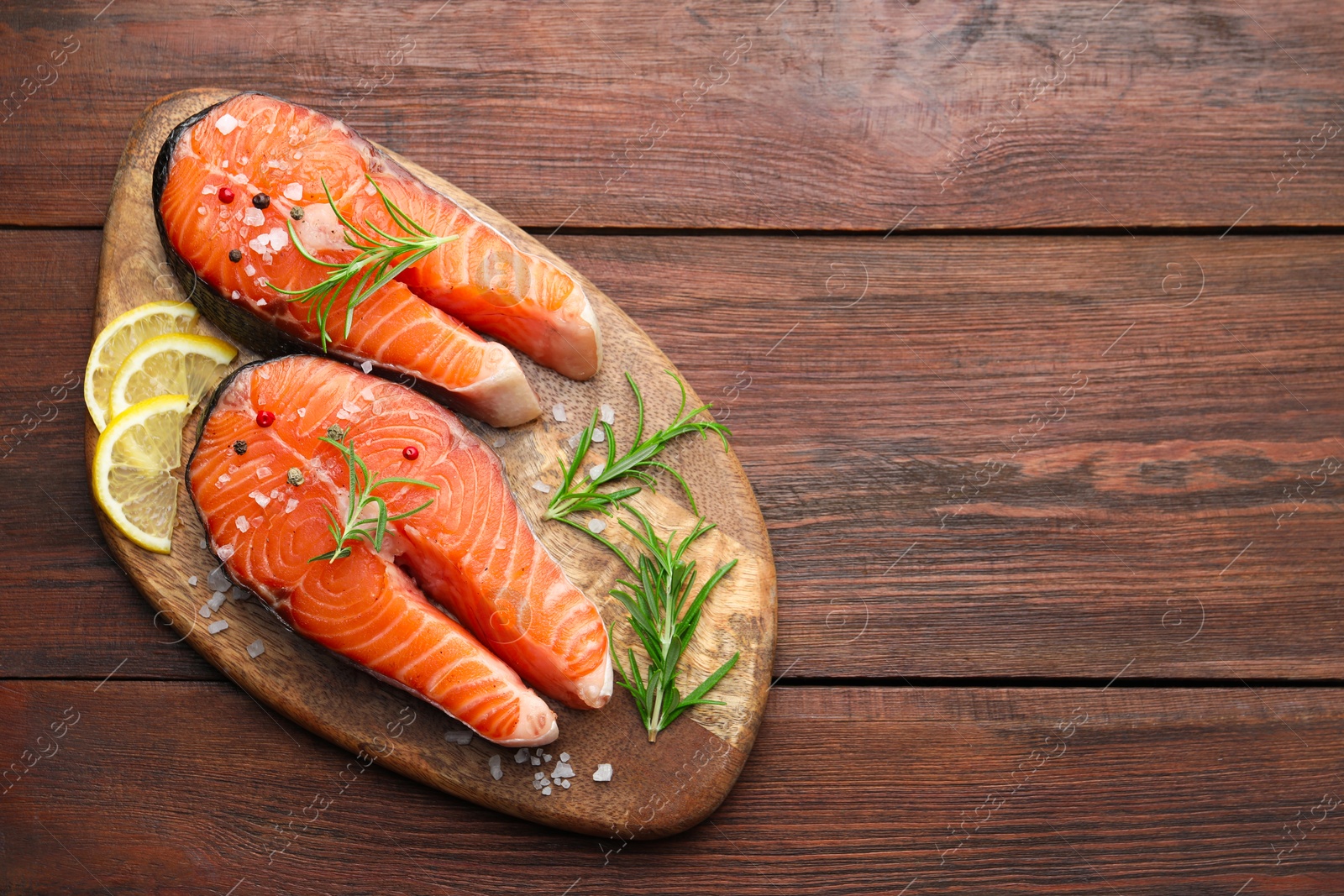 Photo of Fresh raw salmon steaks with spices, lemon and rosemary on wooden table, top view. Space for text