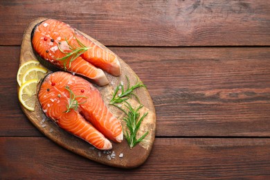 Photo of Fresh raw salmon steaks with spices, lemon and rosemary on wooden table, top view. Space for text