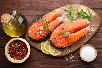 Photo of Fresh raw salmon steaks with spices, lemon, oil and rosemary on wooden table, flat lay