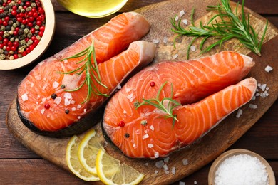 Photo of Fresh raw salmon steaks with spices, lemon and rosemary on wooden table, flat lay