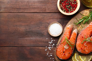 Photo of Fresh raw salmon steaks with spices, lemon and rosemary on wooden table, flat lay. Space for text