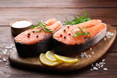 Photo of Fresh raw salmon steaks with spices, lemon and rosemary on wooden table, closeup