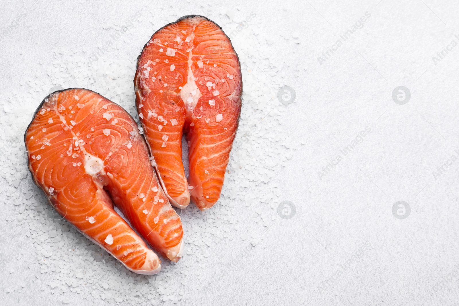 Photo of Fresh raw salmon steaks with salt on light textured table, top view. Space for text