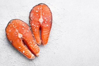 Photo of Fresh raw salmon steaks with salt on light textured table, top view. Space for text