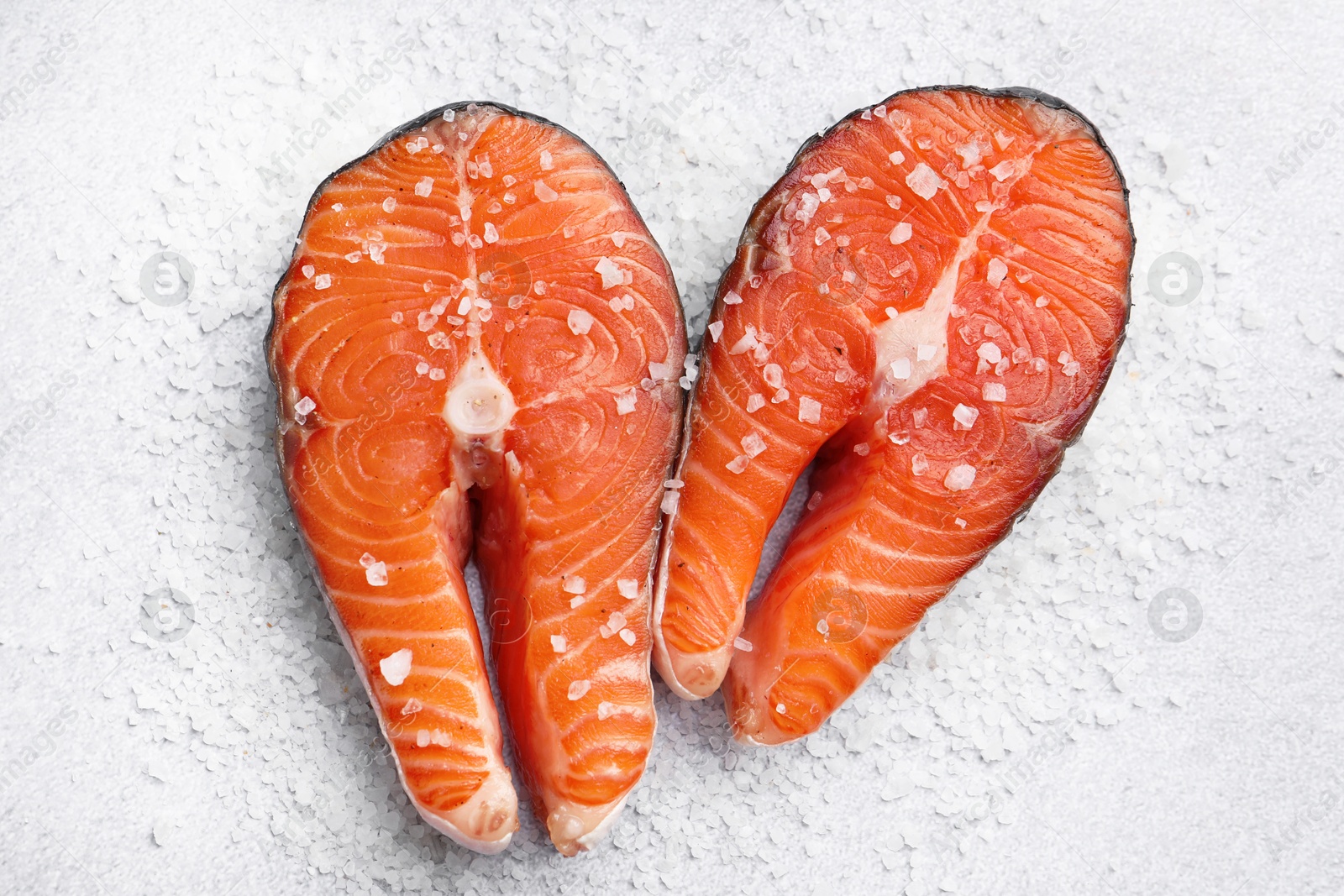 Photo of Fresh raw salmon steaks with salt on light textured table, top view