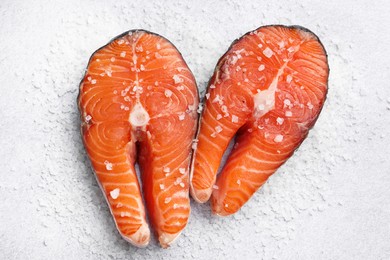 Photo of Fresh raw salmon steaks with salt on light textured table, top view