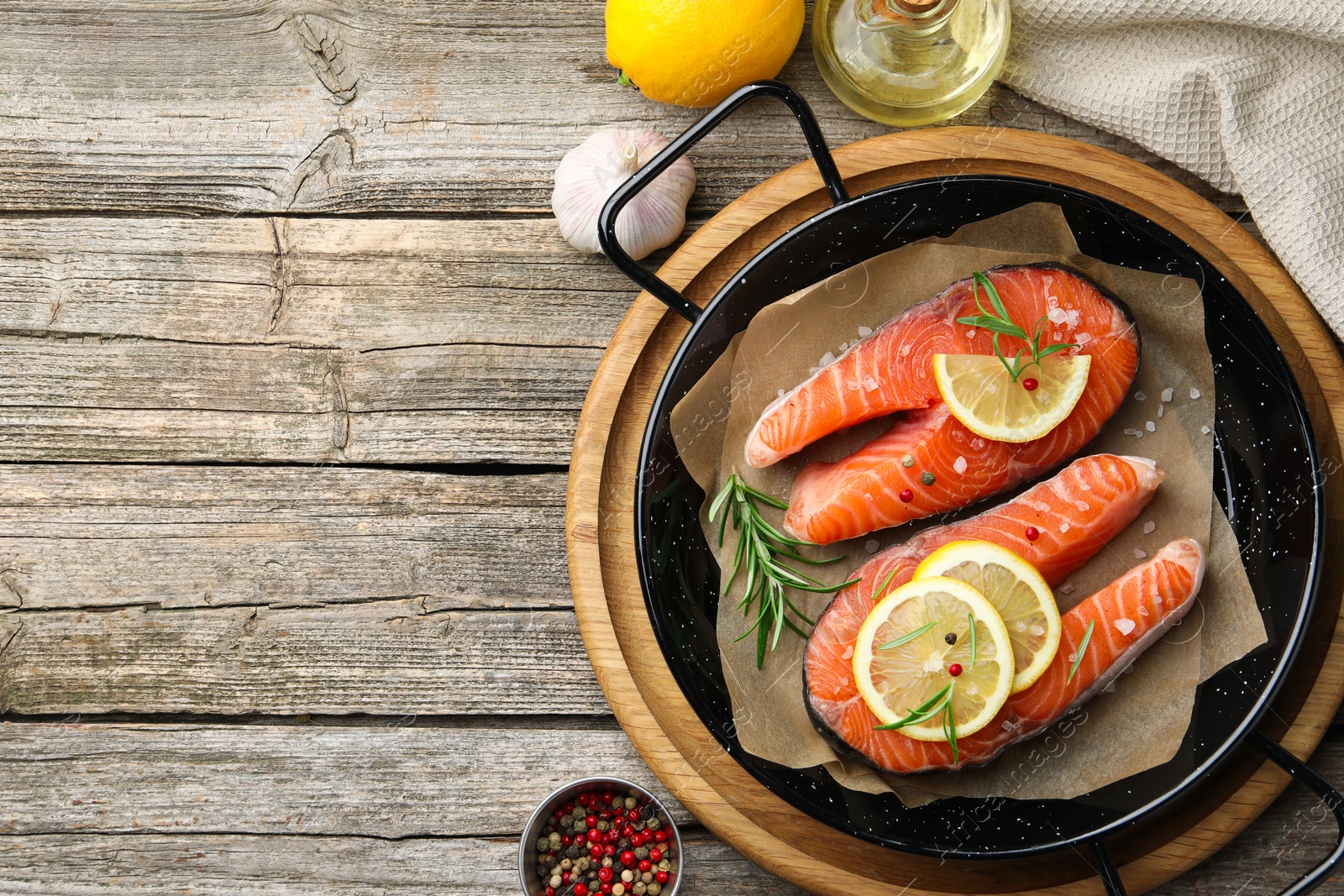 Photo of Fresh raw salmon steaks with spices in pan and products on wooden table, flat lay. Space for text