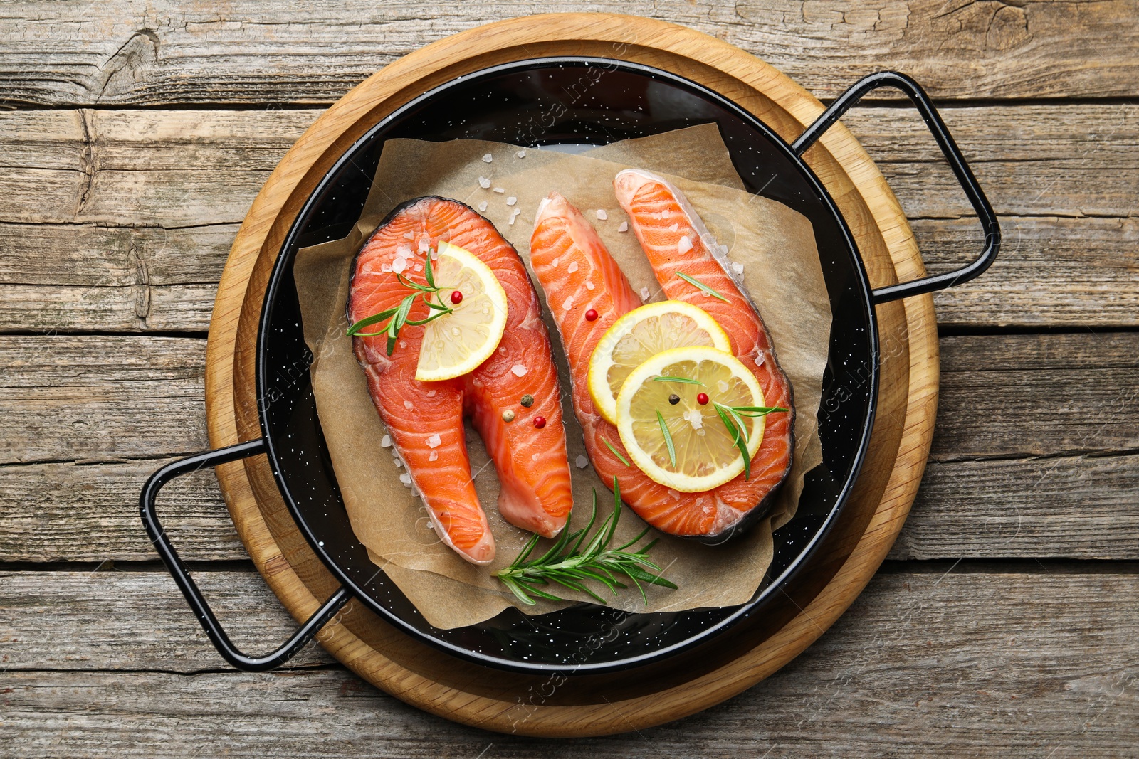 Photo of Fresh raw salmon steaks with spices in pan on wooden table, top view