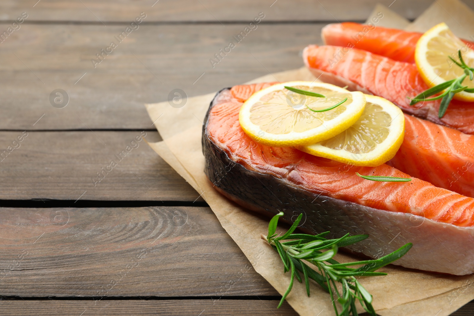 Photo of Fresh raw salmon steaks with rosemary and lemon on wooden table, closeup. Space for text