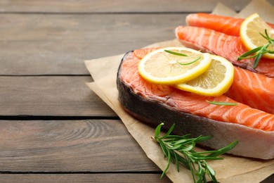 Photo of Fresh raw salmon steaks with rosemary and lemon on wooden table, closeup. Space for text