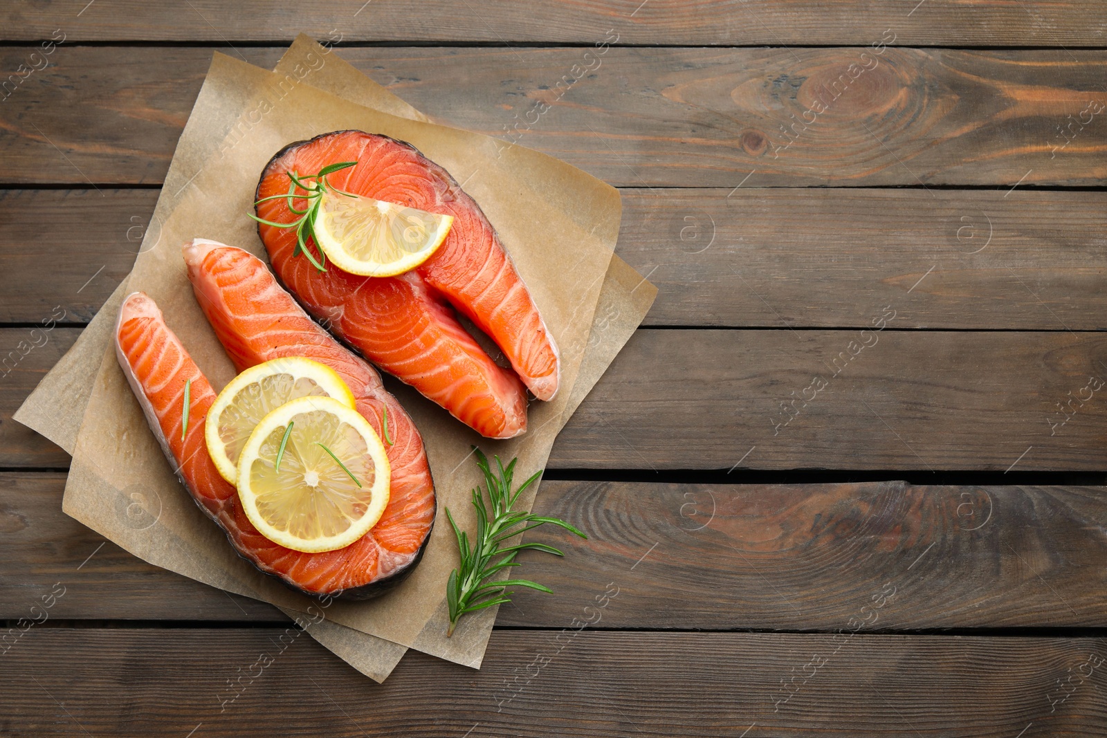 Photo of Fresh raw salmon steaks with rosemary and lemon on wooden table, top view. Space for text