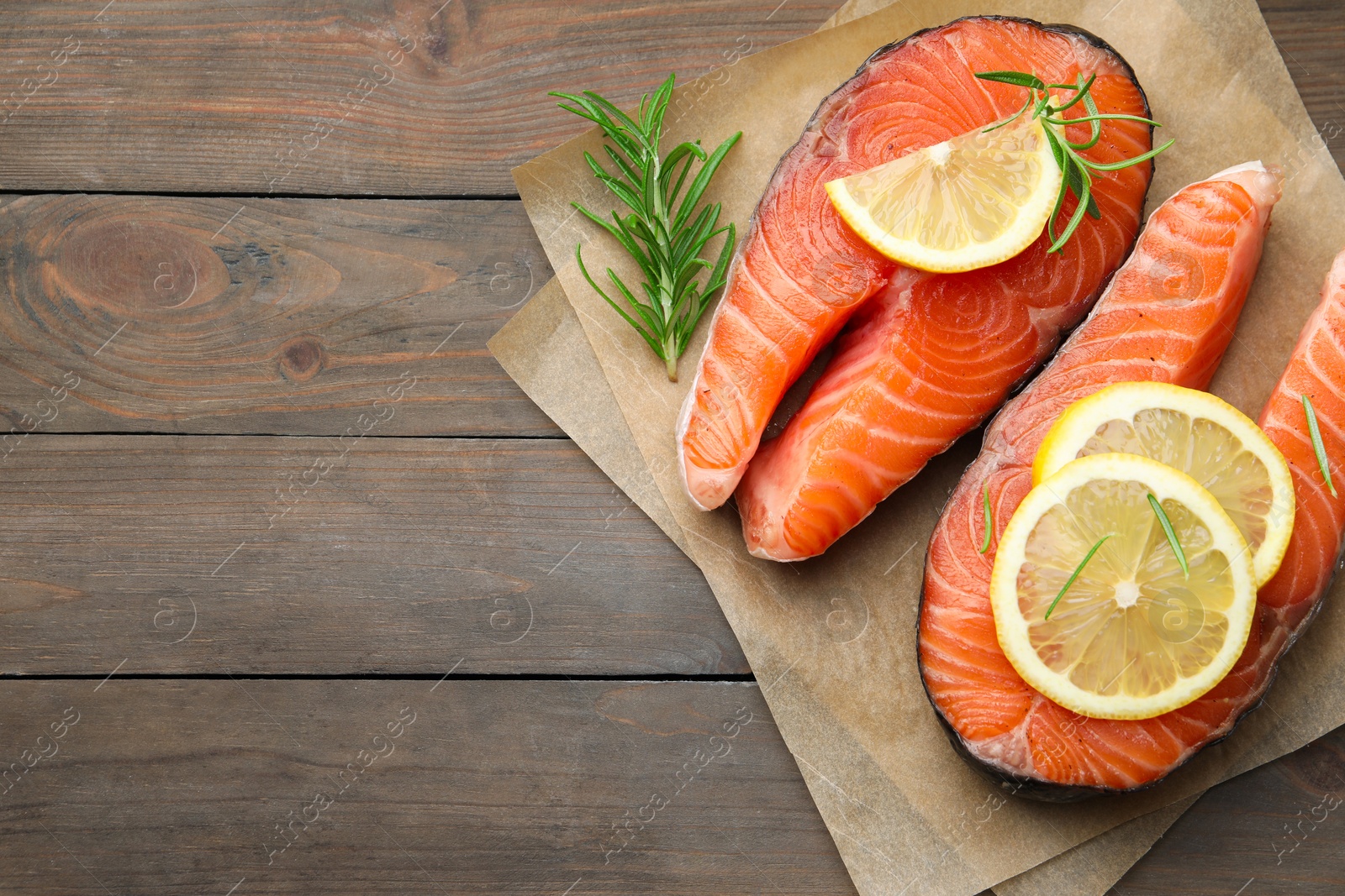 Photo of Fresh raw salmon steaks with rosemary and lemon on wooden table, top view. Space for text