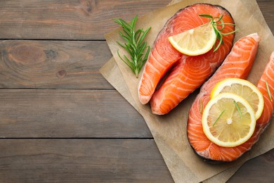 Photo of Fresh raw salmon steaks with rosemary and lemon on wooden table, top view. Space for text