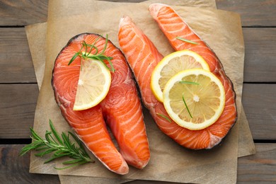 Photo of Fresh raw salmon steaks with rosemary and lemon on wooden table, top view