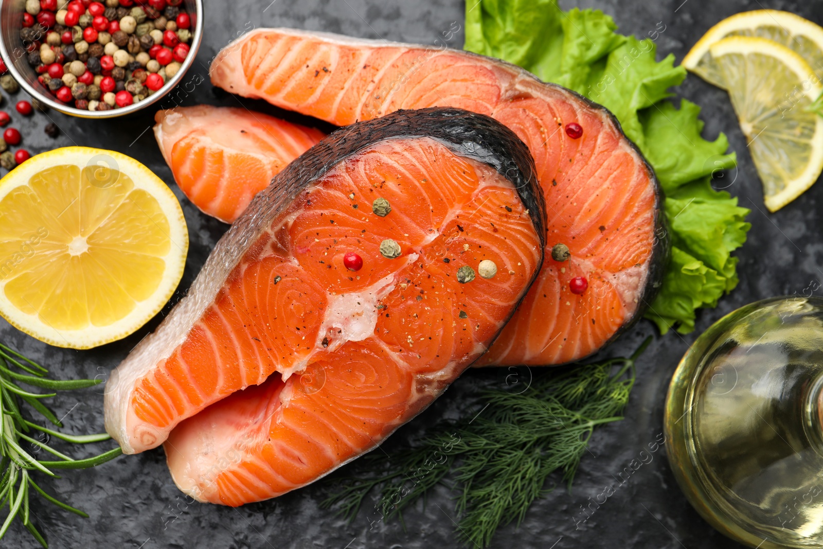 Photo of Fresh raw salmon steaks with spices and products on dark textured table, above view