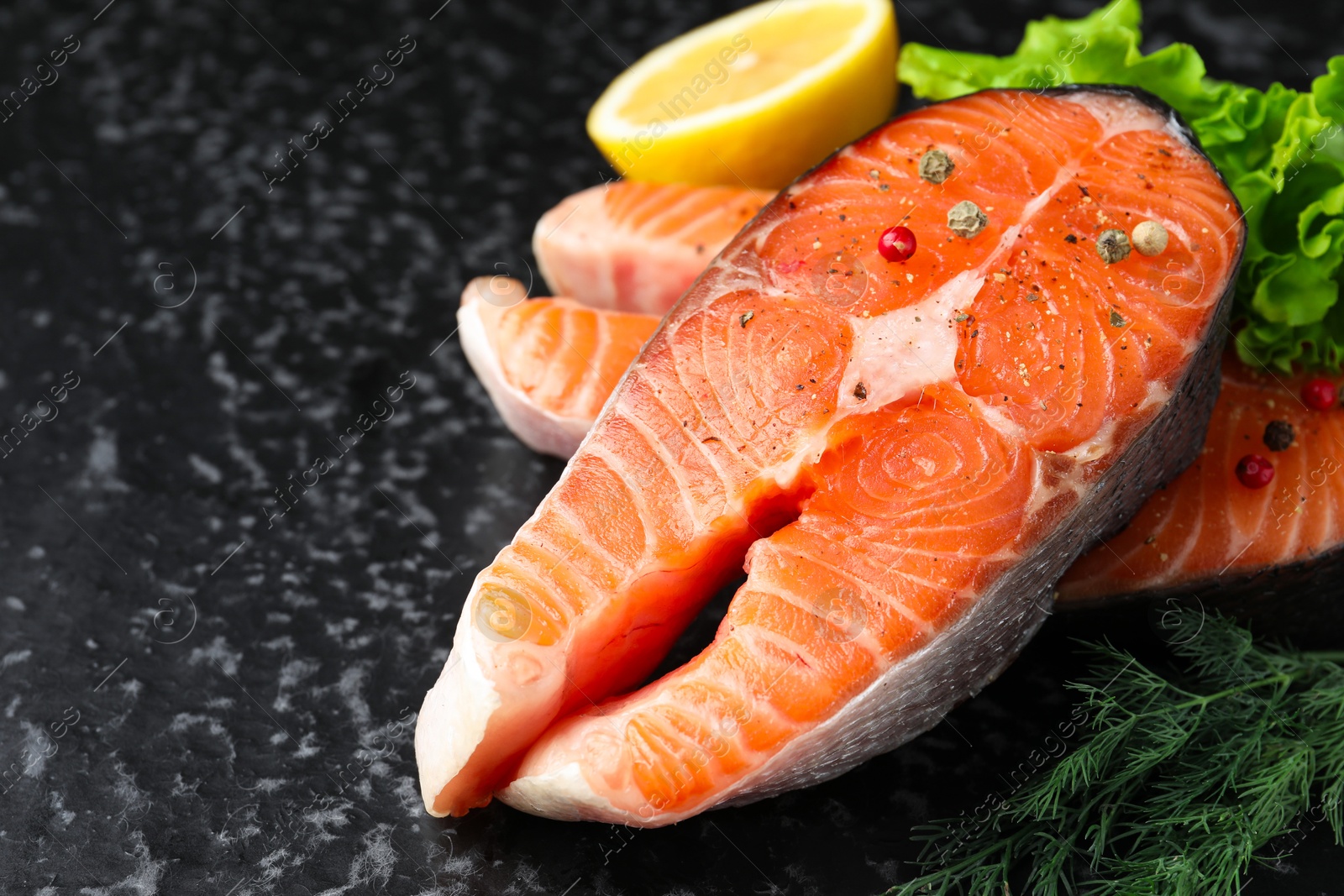 Photo of Fresh raw salmon steaks with spices, lemon, lettuce and dill on dark textured table, closeup. Space for text