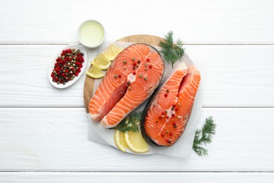 Photo of Fresh raw salmon steaks with peppercorns, lemon, oil and dill on white wooden table, flat lay