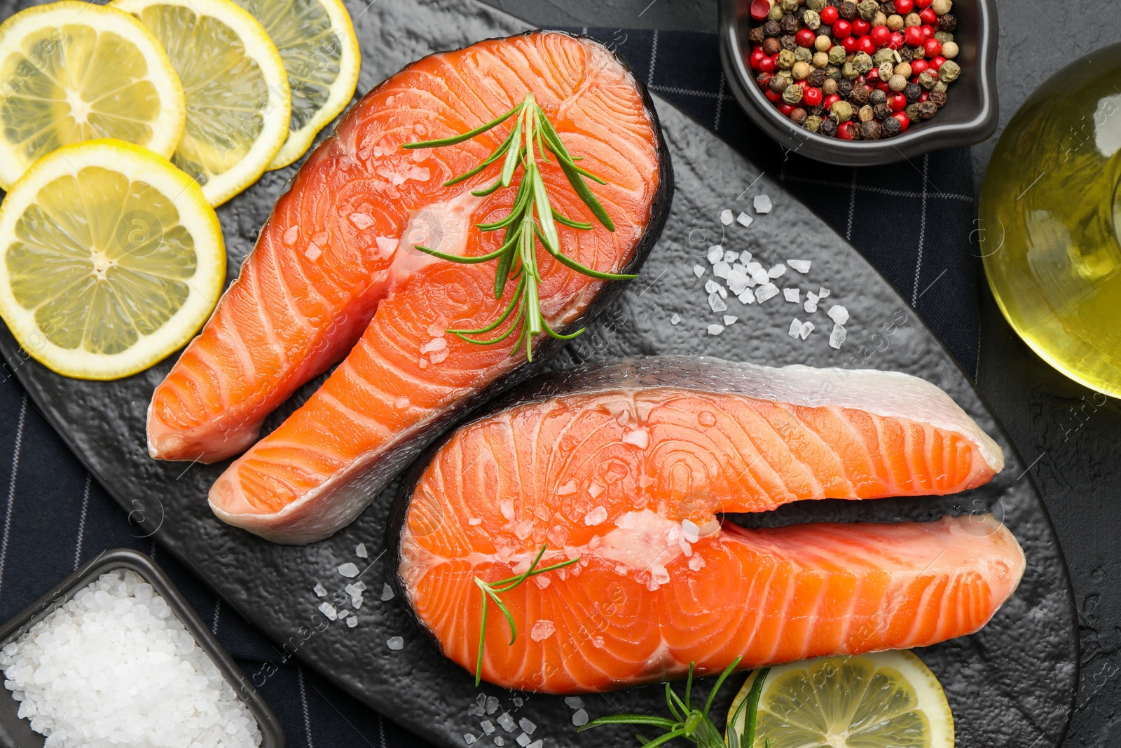 Photo of Fresh raw salmon steaks with salt, lemon and rosemary on dark table, flat lay