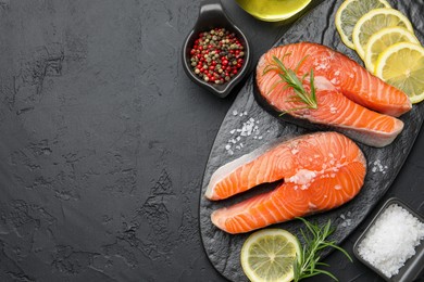 Photo of Fresh raw salmon steaks with salt, lemon, peppercorns and rosemary on dark textured table, flat lay. Space for text