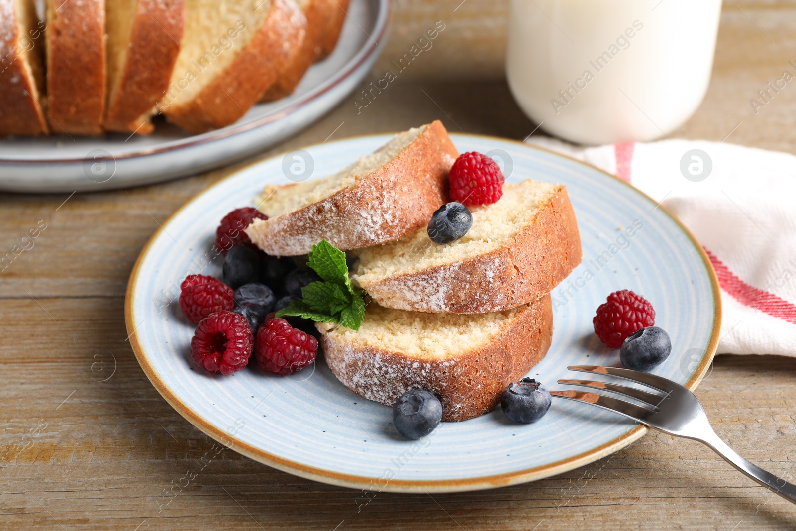 Photo of Pieces of freshly baked sponge cake, berries and milk on wooden table, closeup