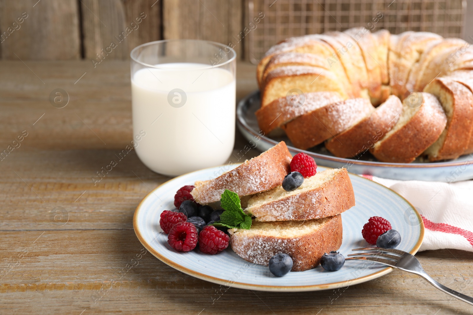 Photo of Pieces of freshly baked sponge cake, berries and milk on wooden table, closeup