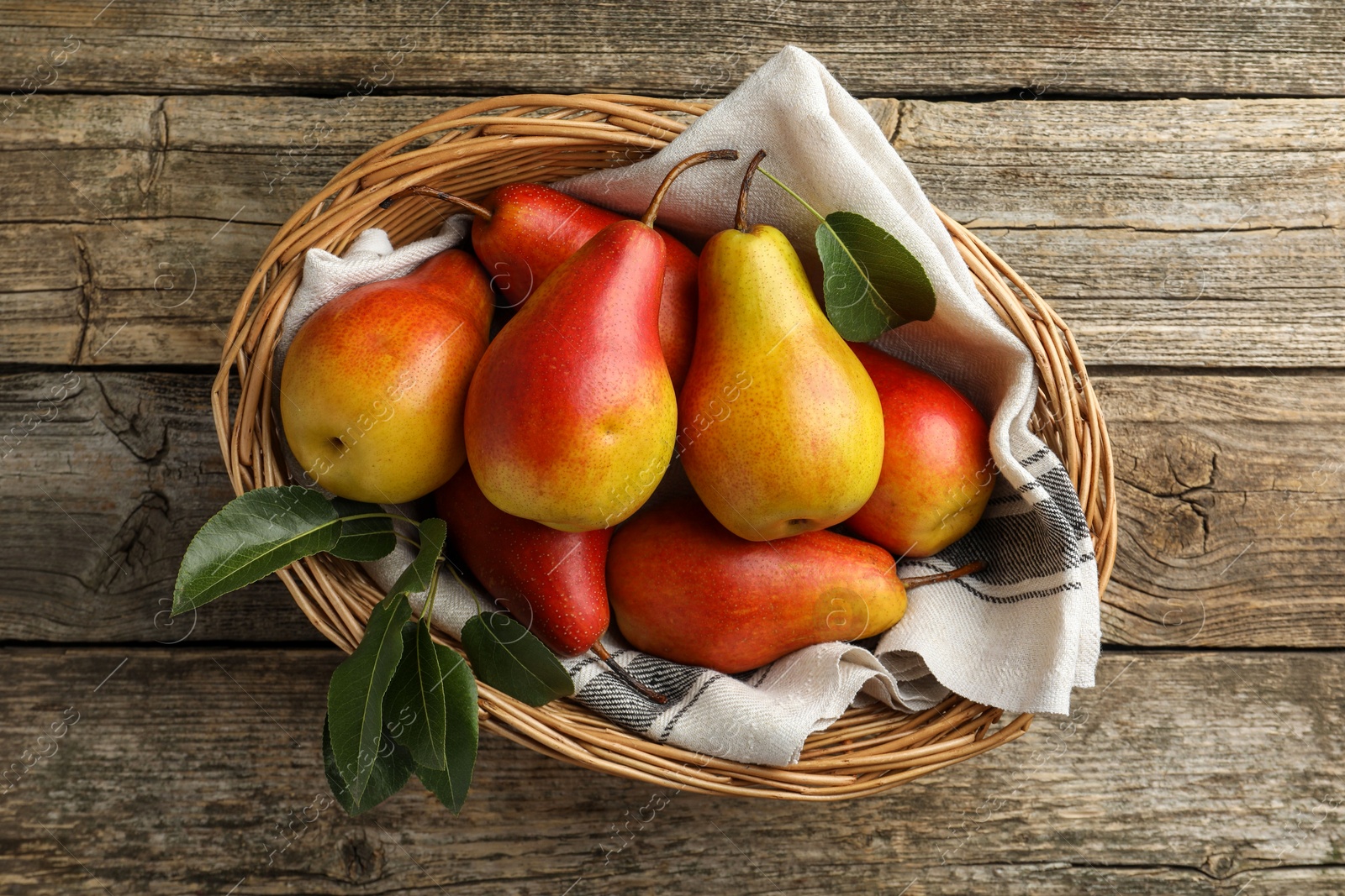 Photo of Ripe juicy pears in wicker basket on wooden table, top view