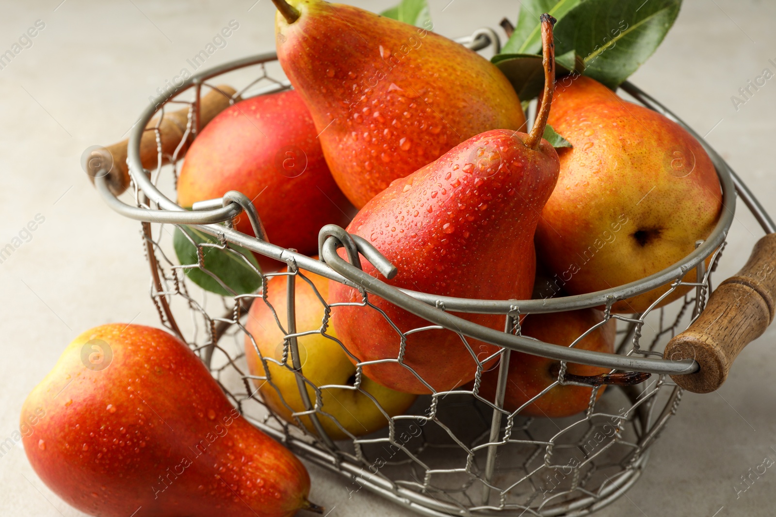 Photo of Ripe juicy pears in metal basket on grey textured table, closeup