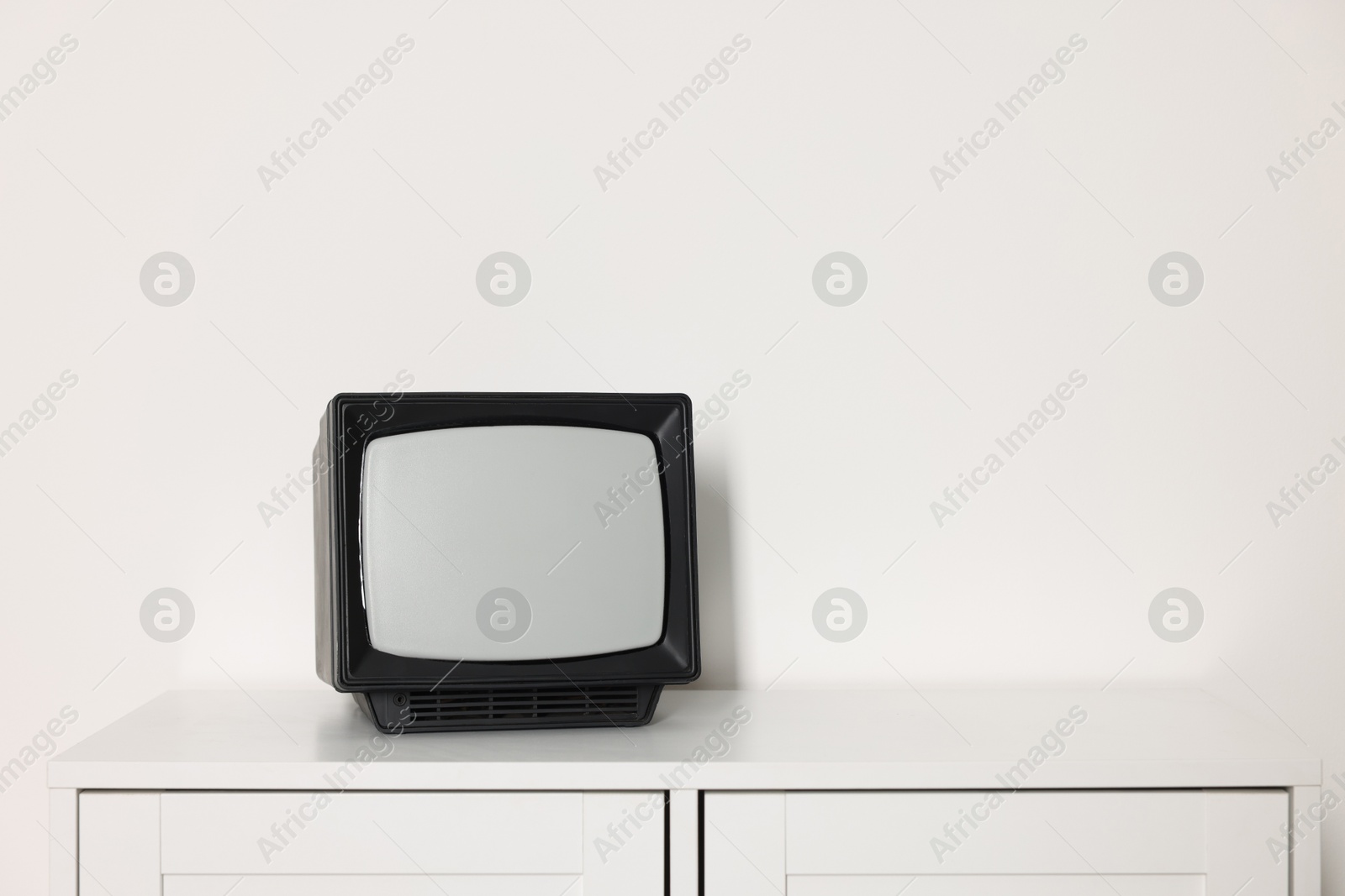 Photo of Retro tv set on chest of drawers against white wall. Space for text