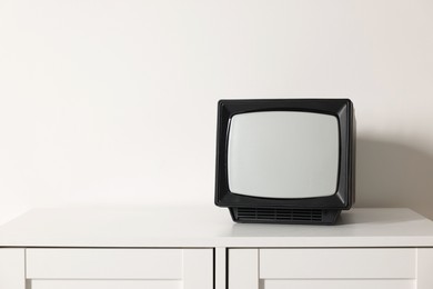 Photo of Retro tv set on chest of drawers against white wall. Space for text