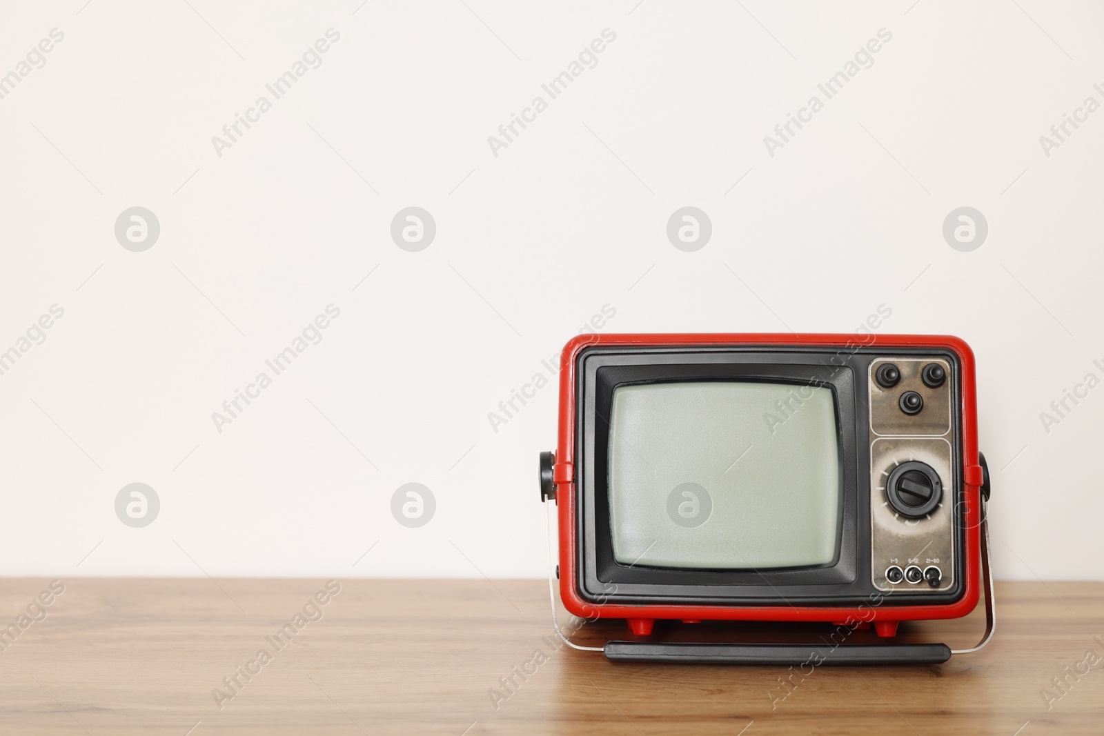 Photo of Retro tv set on wooden shelf against white wall. Space for text