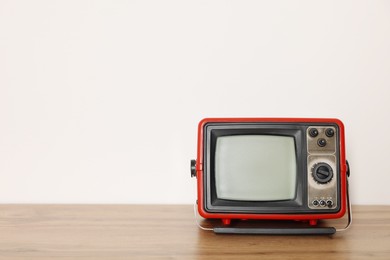 Photo of Retro tv set on wooden shelf against white wall. Space for text