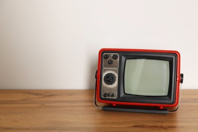 Photo of Retro tv set on wooden shelf against white wall. Space for text