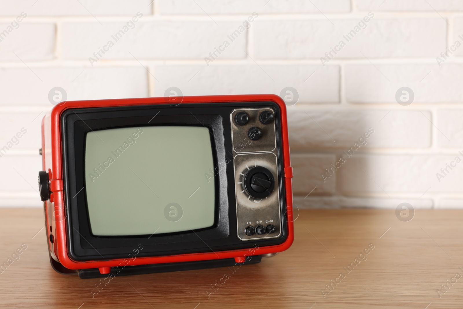 Photo of Retro tv set on wooden shelf against white brick wall. Space for text