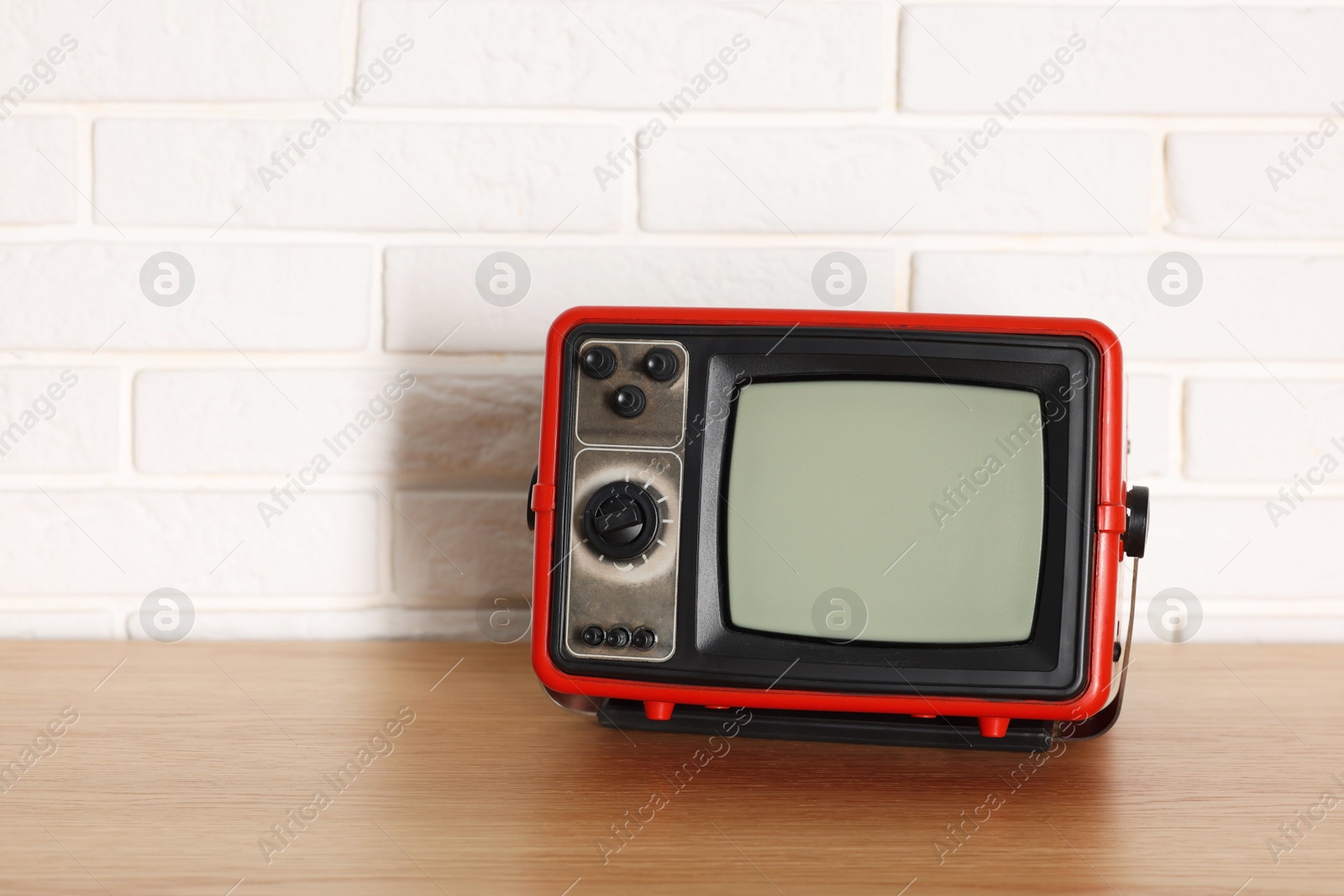 Photo of Retro tv set on wooden shelf against white brick wall. Space for text