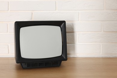 Photo of Retro tv set on wooden shelf against white brick wall. Space for text