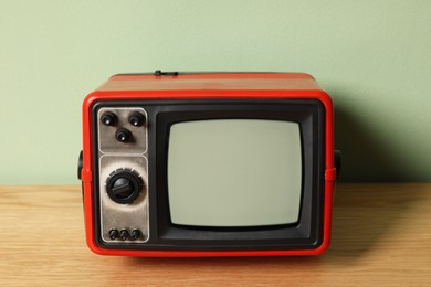 Photo of Retro tv set on wooden shelf against green wall