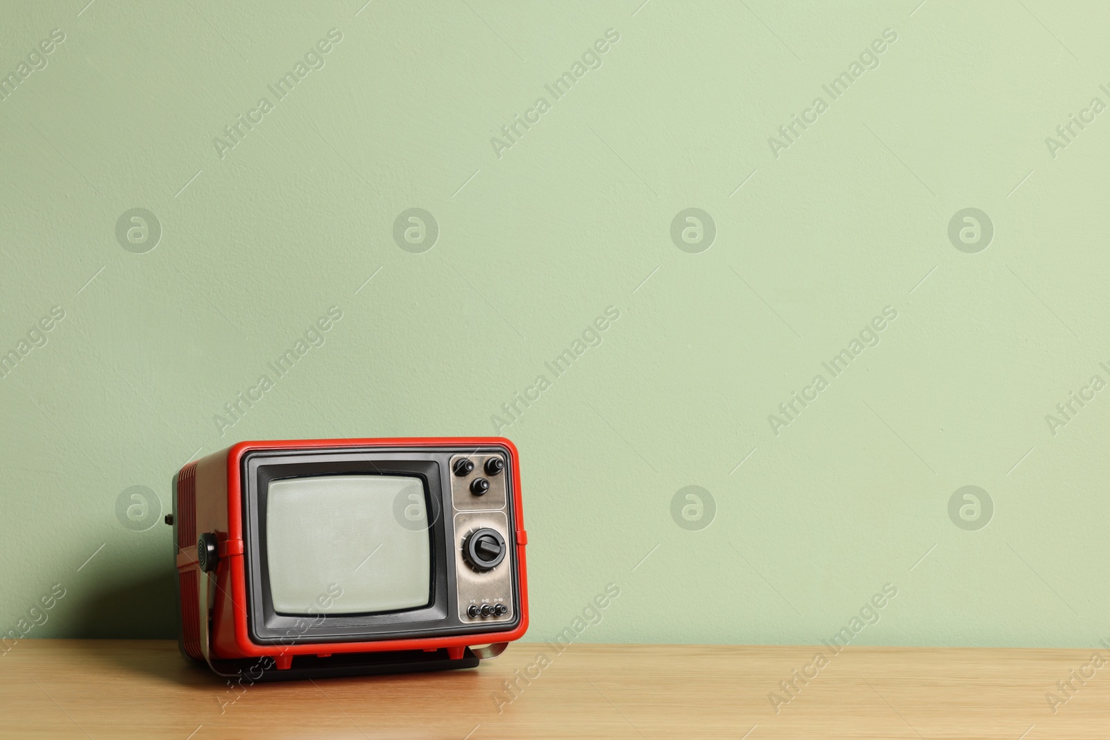 Photo of Retro tv set on wooden shelf against green wall. Space for text