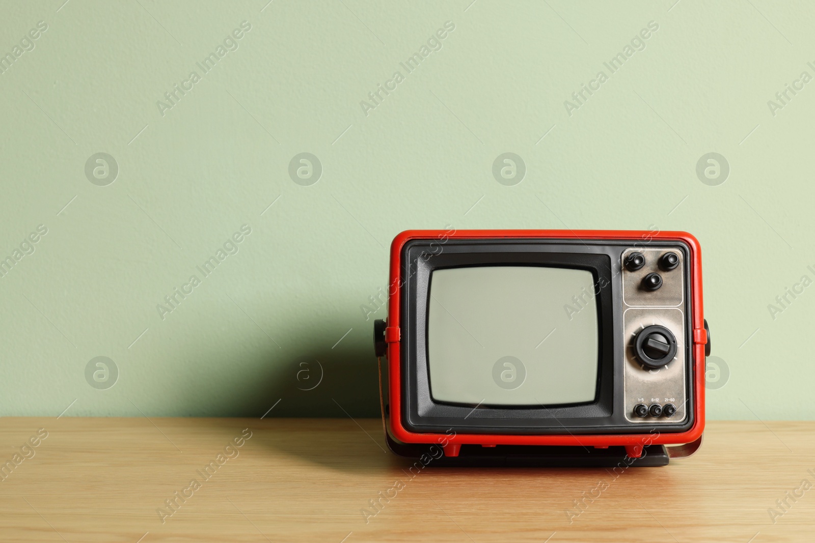 Photo of Retro tv set on wooden shelf against green wall. Space for text