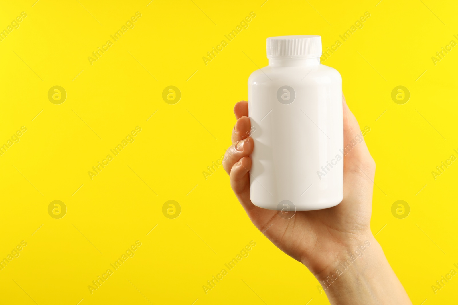 Photo of Woman holding medical bottle with pills on yellow background, closeup. Space for text