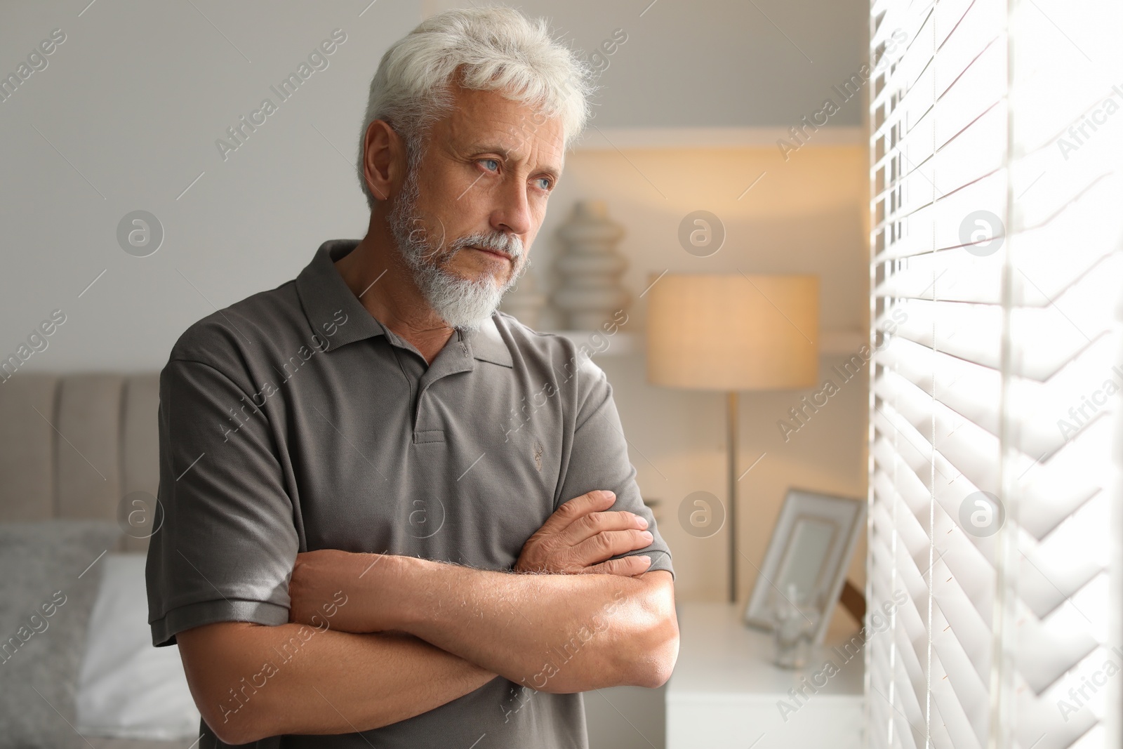 Photo of Lonely senior man looking out window indoors