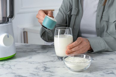 Photo of Making protein cocktail. Woman adding powder into glass with milk at white marble table, closeup