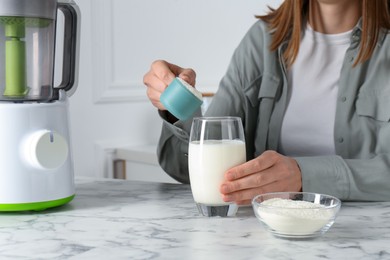 Photo of Making protein cocktail. Woman adding powder into glass with milk at white marble table, closeup