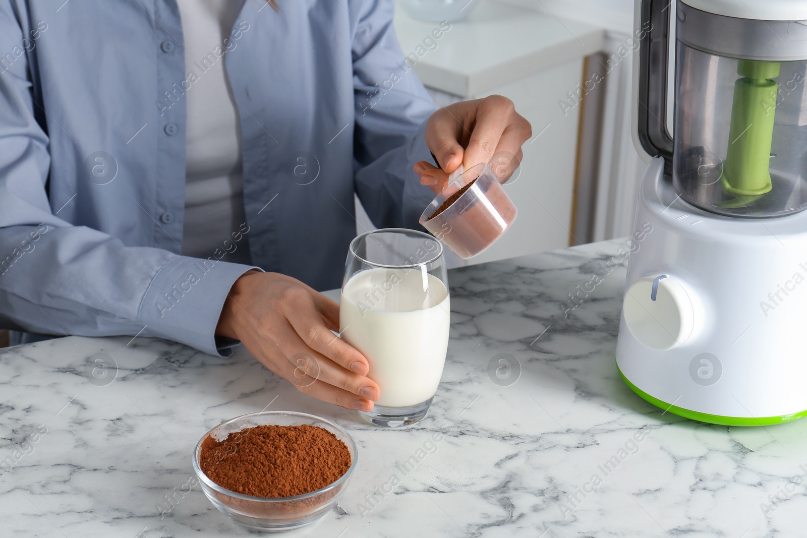 Photo of Making protein cocktail. Woman adding powder into glass with milk at white marble table, closeup